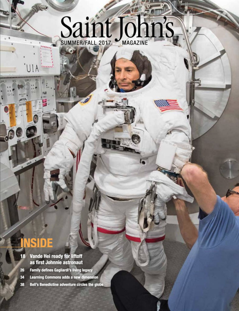 An astronaut in a white spacesuit is being assisted by a person in blue inside a spacecraft. The interior is equipped with various instruments. The cover text reads, "Saint John's Magazine, Summer/Fall 2017.